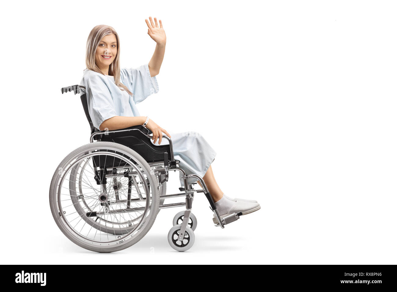 Smiling female patient in a wheelchair waving at the camera isolated on white background Stock Photo
