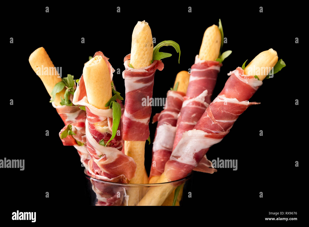 Prosciutto wrapped around grissini breadsticks. Black background Stock