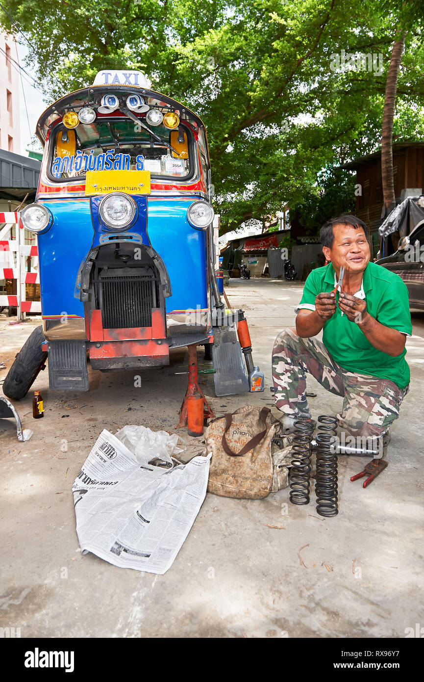 Bangkok, Thailand: Close-up of one colorful Tuk-Tuk vehicle, isolated from other traffic, under repair on the street by its driver Stock Photo