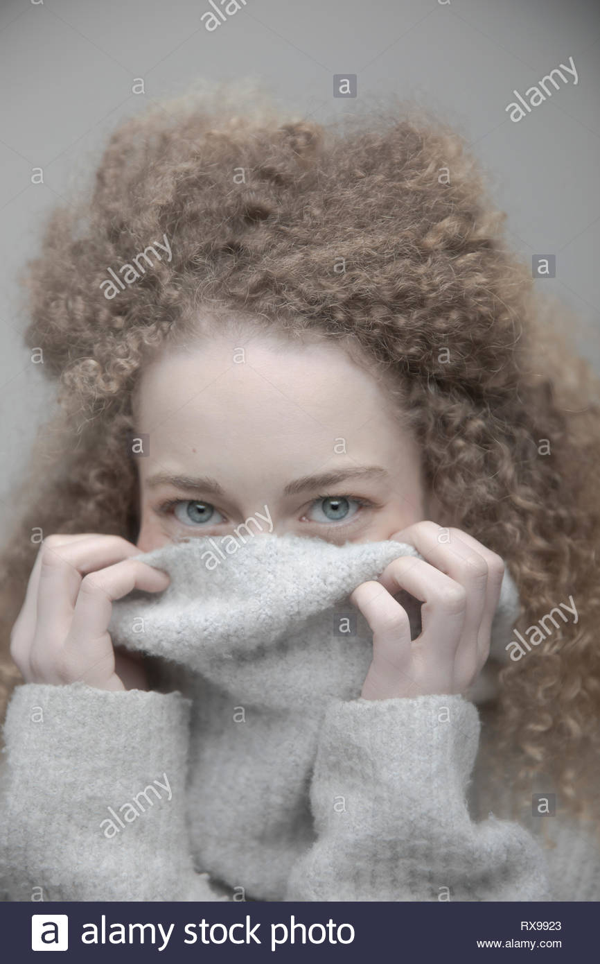 Portrait playful beautiful young blonde woman with curly long hair hiding in sweater Stock Photo