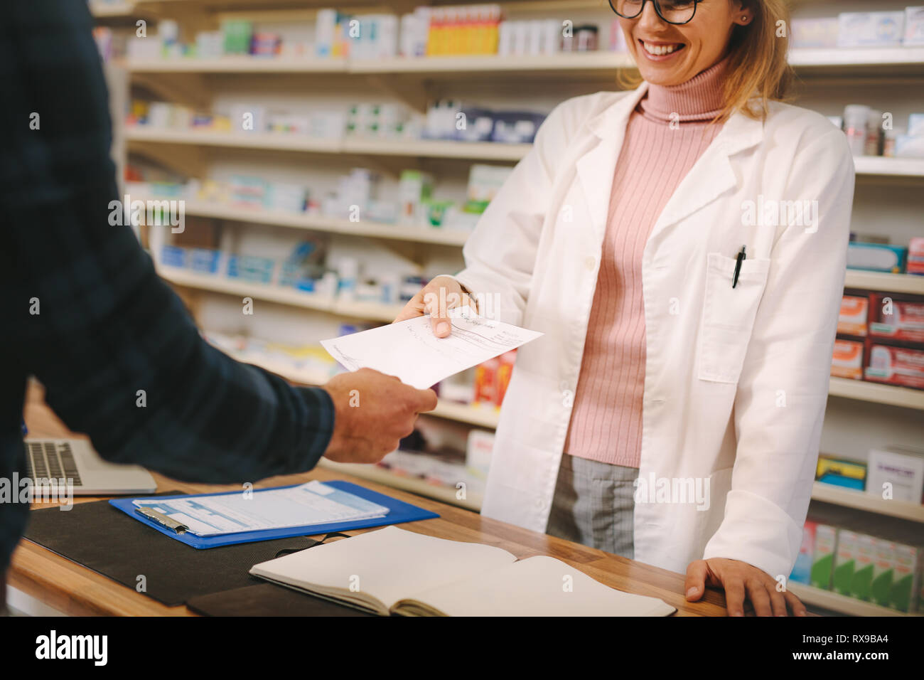 Female apothecary taking prescription from customer at pharmacy. Customer handing a medical prescription to the pharmacist standing behind counter. Stock Photo