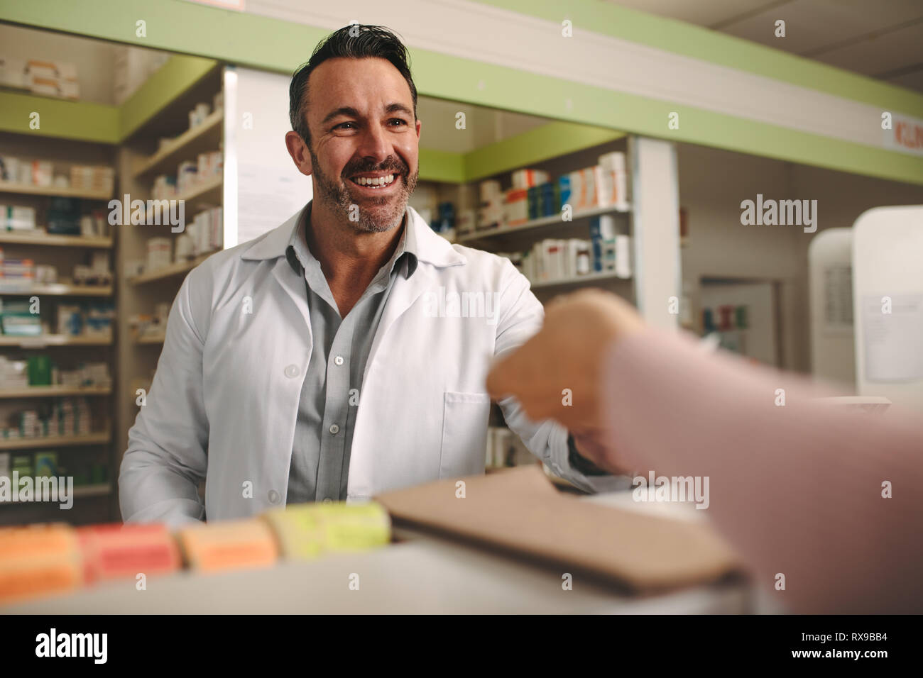 Customer handing a medical prescription to the smiling male chemist standing behind counter. Chemist taking prescription from customer at drugstore. Stock Photo