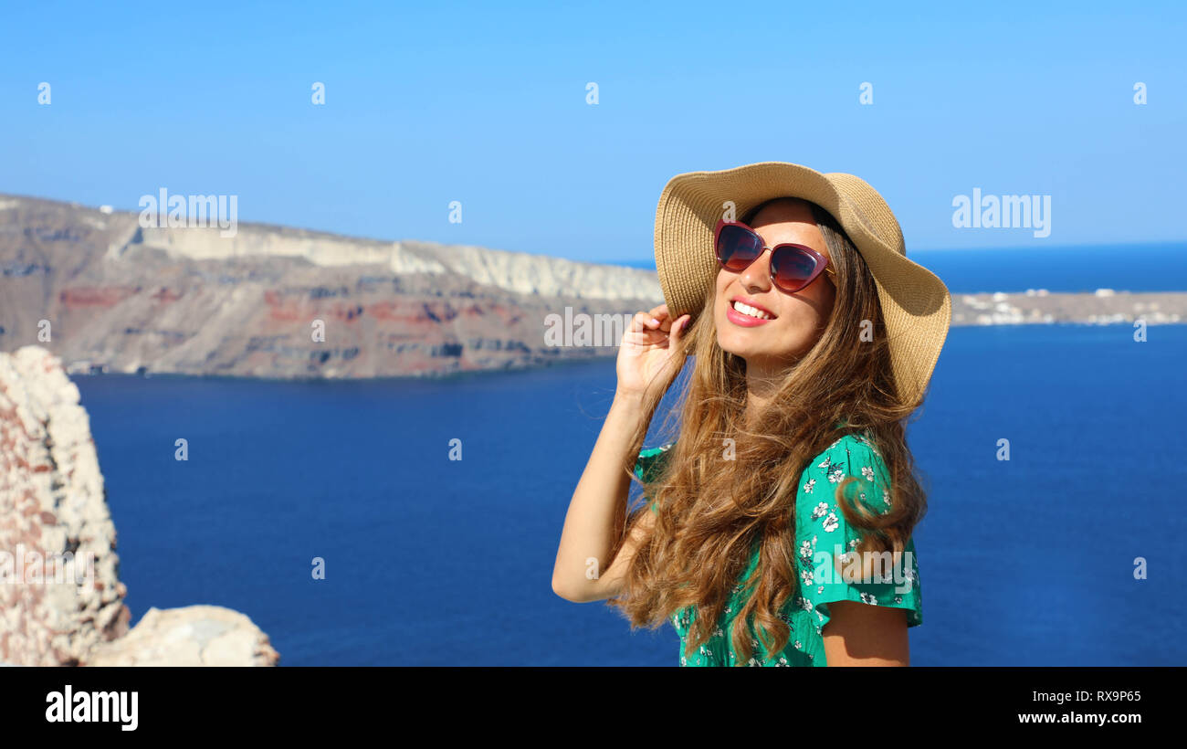 Beautiful young woman with hat and sunglasses enjoying the sun in Santorini with the Caldera on background, Greece, Europe Stock Photo