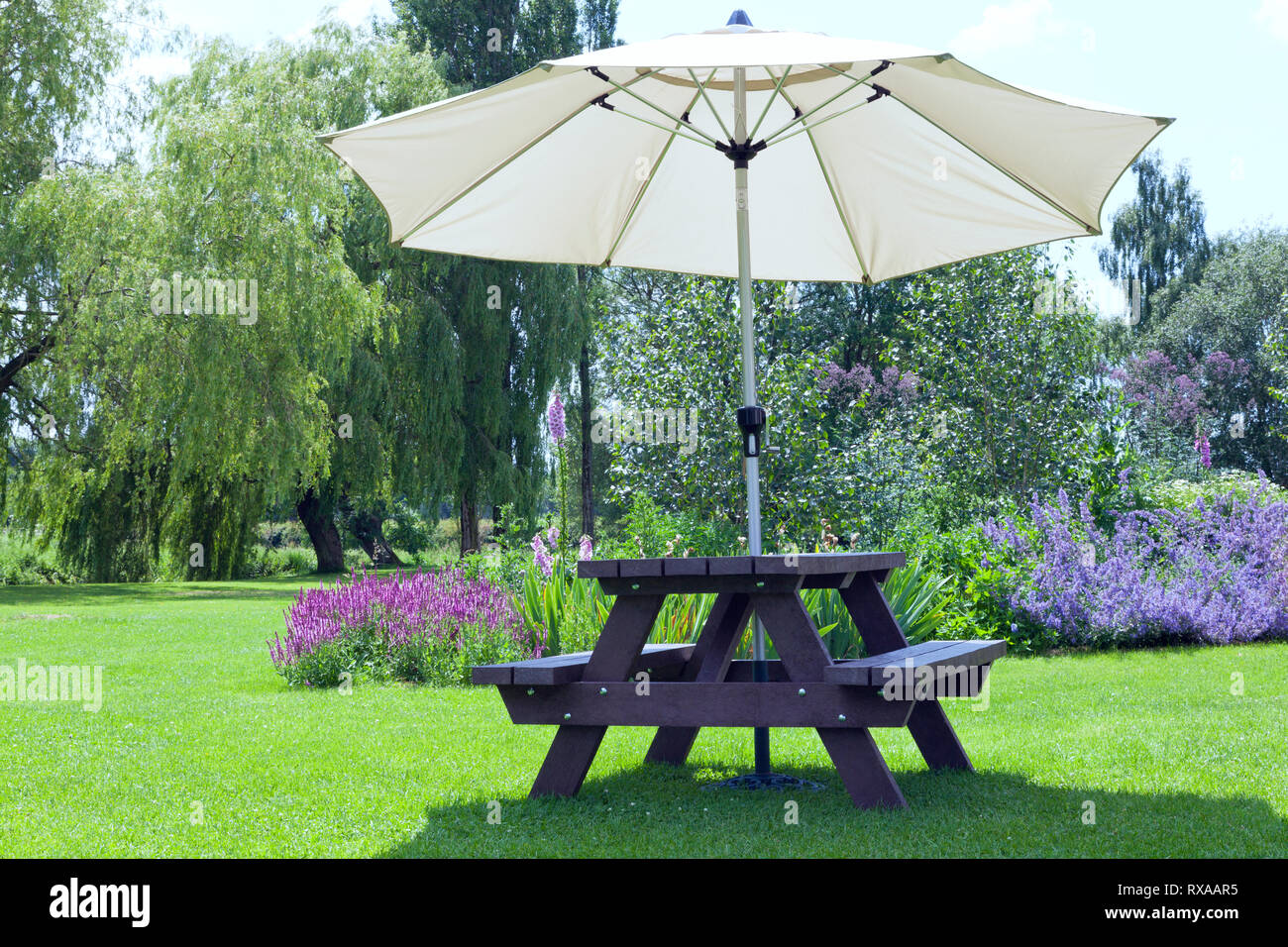 Relaxing Setting In A Pub Garden With Umbrella Sitting Bench Next To Flowers In Bloom