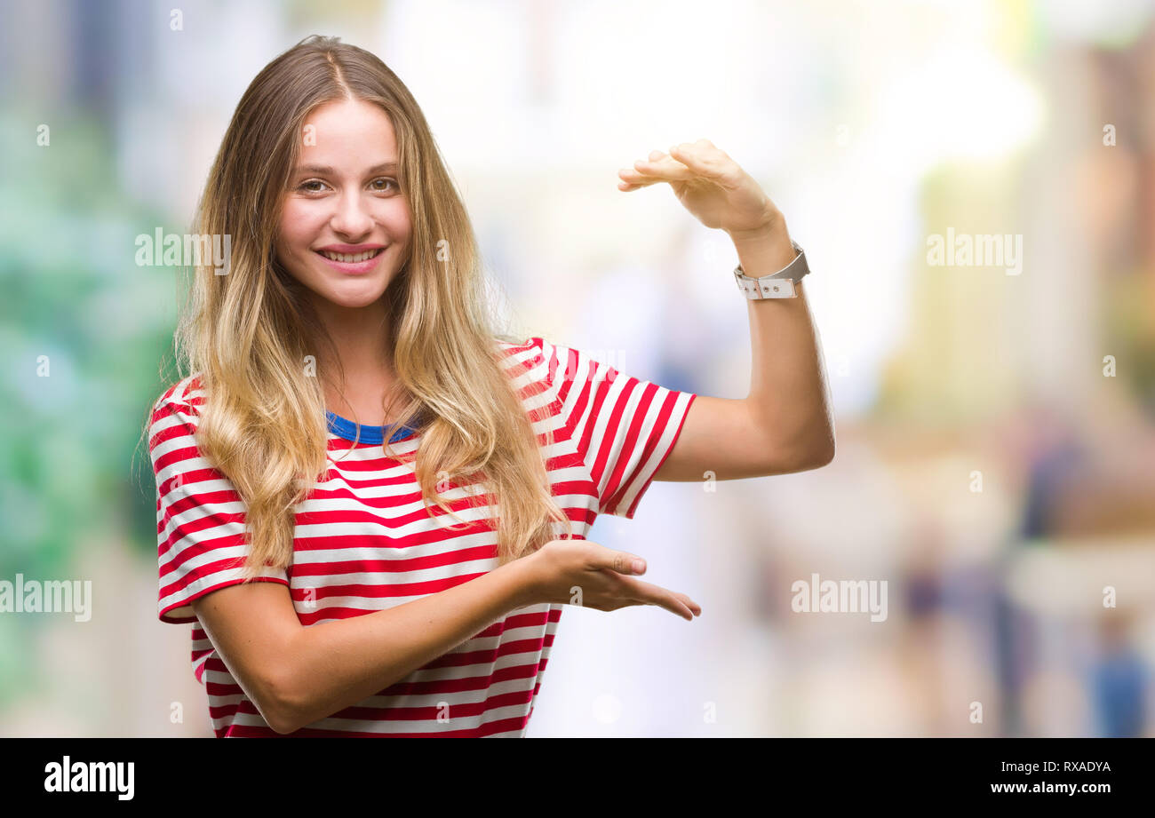 Young beautiful blonde woman over isolated background gesturing with hands showing big and large size sign, measure symbol. Smiling looking at the cam Stock Photo