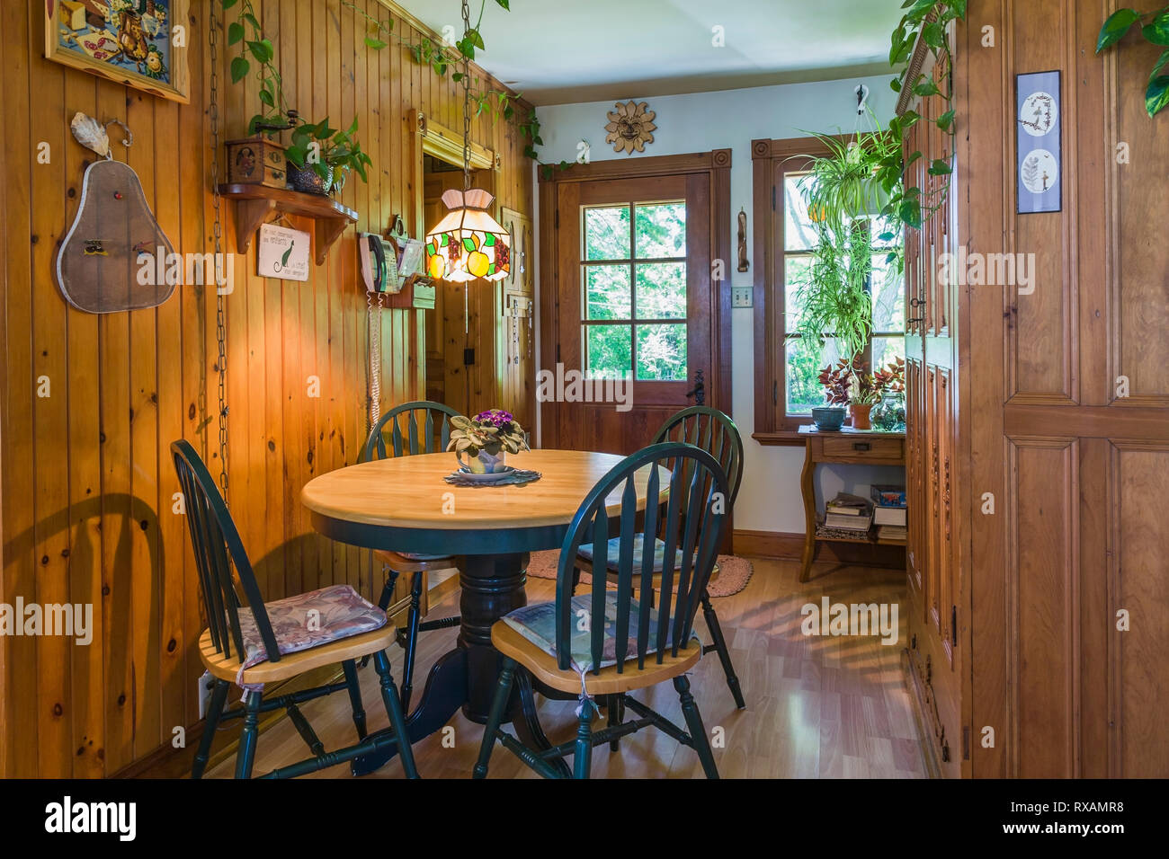 Country kitchen with cherrywood dining table and high back chairs, pinewood cabinets, wood laminate floor inside an old 1927 Canadiana cottage style home, Quebec, Canada. This image is property released. CUPR0321 Stock Photo