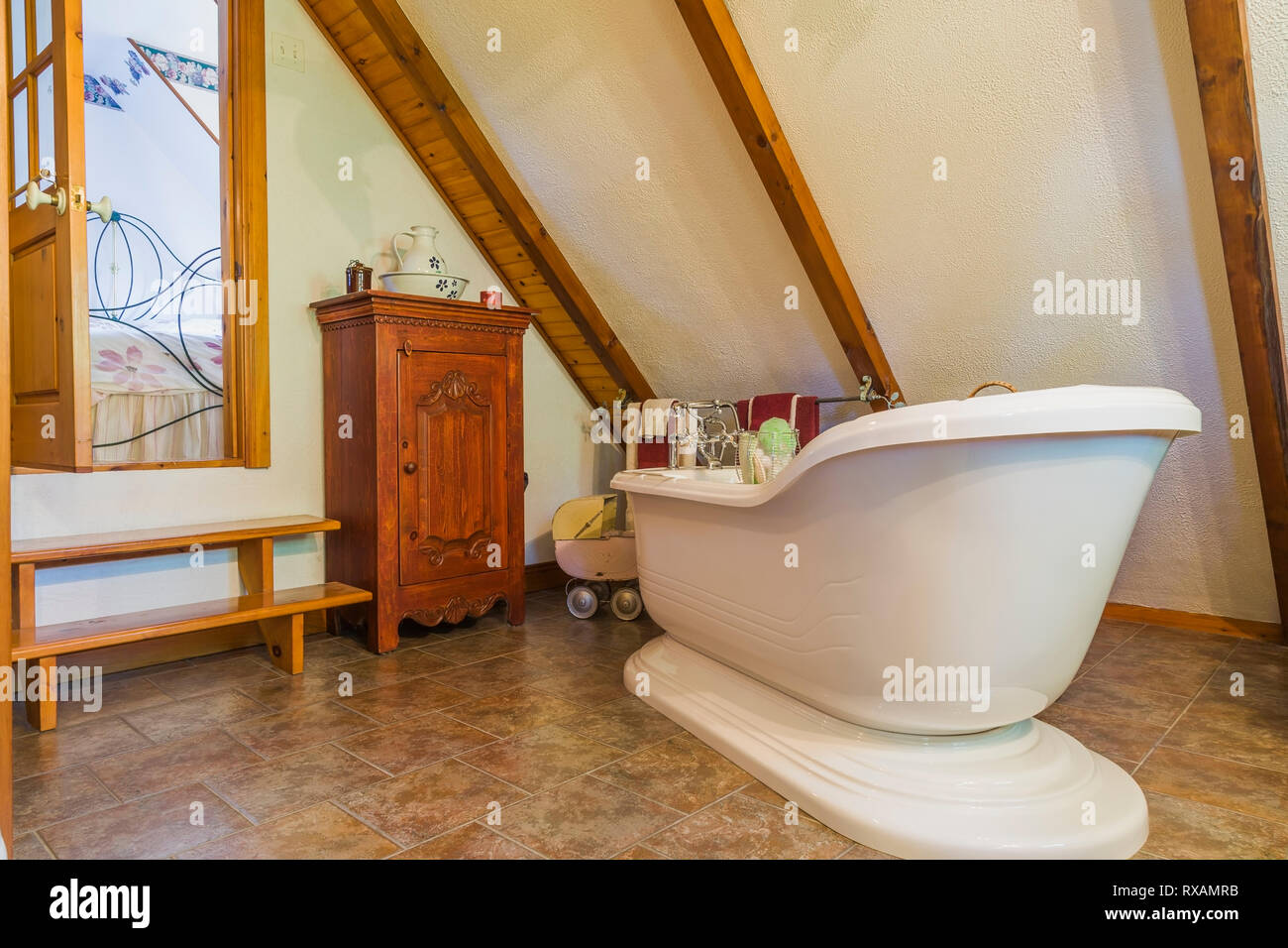 White freestanding Alcove bathtub with small wooden armoire in en suite on upstairs floor inside an old 1927 Canadiana cottage style home, Quebec, Canada. This image is property released. CUPR0321 Stock Photo