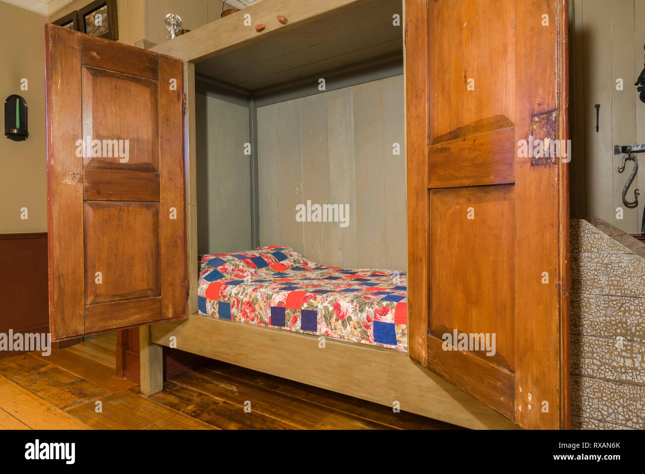 Single bed hidden in an old wooden armoire in the dining room inside an old circa 1805 Canadiana cottage style home, Quebec, Canada. This image is property released. CUPR0323 Stock Photo