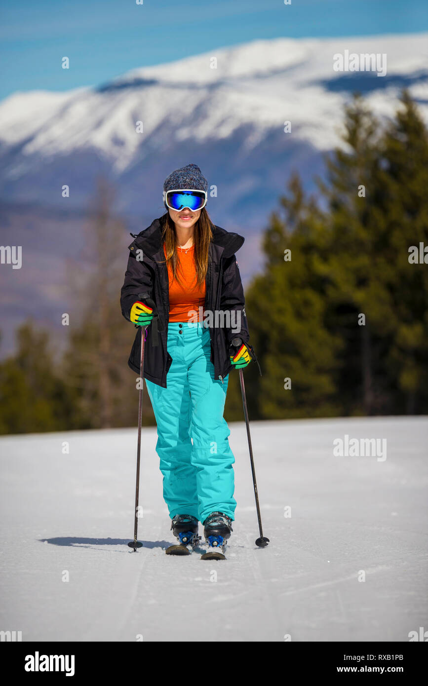 Woman with skies walking on snow covered field against mountain in forest Stock Photo