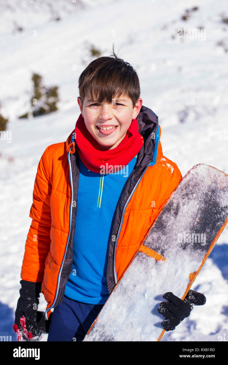 Portrait of boy sticking out tongue while holding snowboard on snowcapped mountain during winter Stock Photo