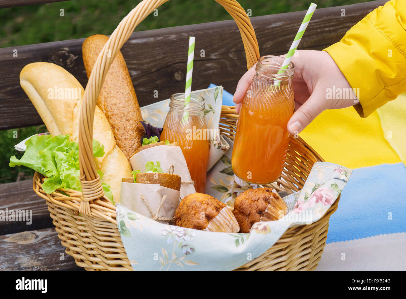 Picnic basket with food and drinks on a park bench and a person holding ...