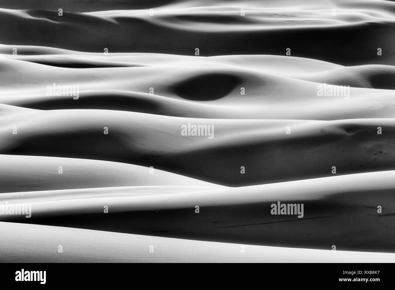 Greyscale impression of simple shapes formed by sun light and shades on endless waves of sand dunes in arid lifeless desert of Australian Pacific coas Stock Photo