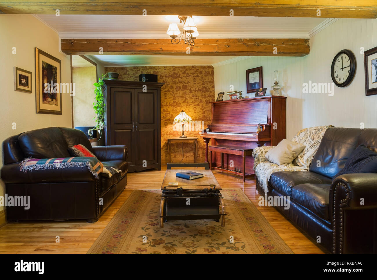 Music room with dark brown leather sofas, upright piano, wooden armoire and old grain scale table inside an old circa 1752 Canadiana style fieldstone house, Quebec, Canada. This image is property released. CUPR0313 Stock Photo