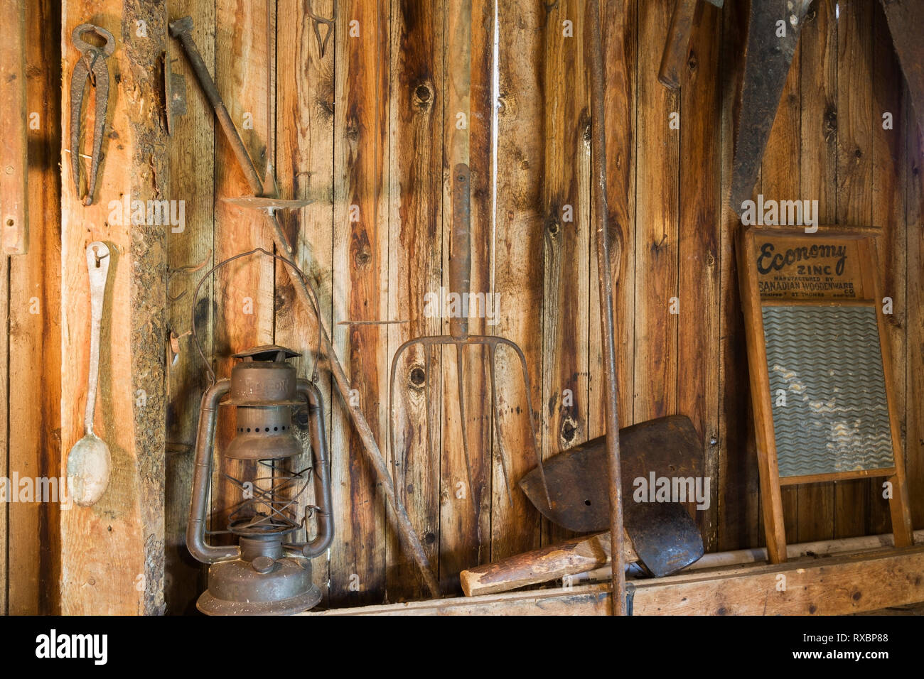 Antique oil lantern, pitchfork, shears, axe, saws, washboard and other manual toolshanging on vertical wood plank wall inside an old barn, Quebec, Canada. This image is property released. CUPR0332 Stock Photo