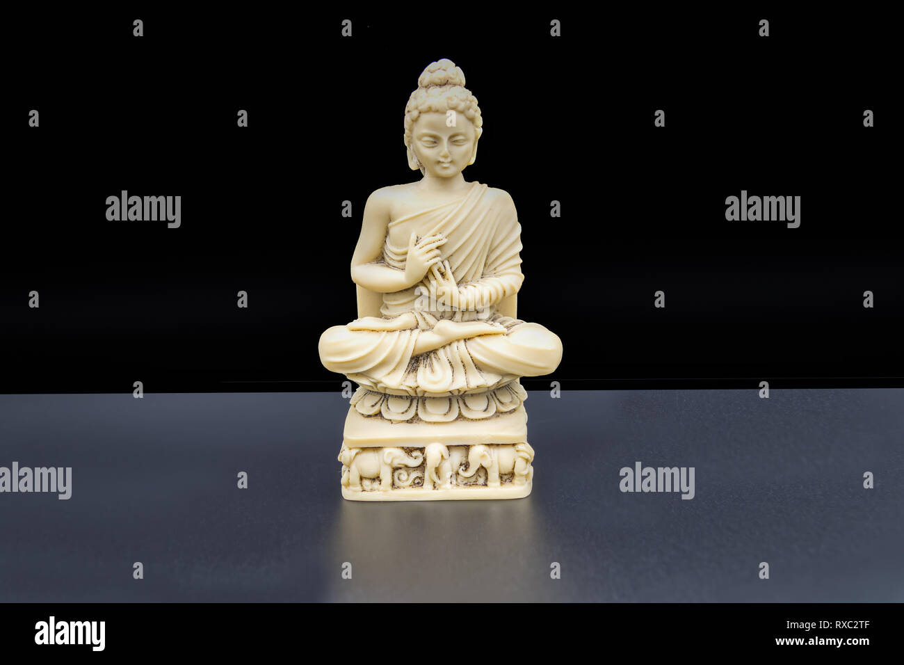 Resolutely train yourself to be at one with peace and harmony.  A Buddha statuette sitting in the lotus position on a black background. Stock Photo