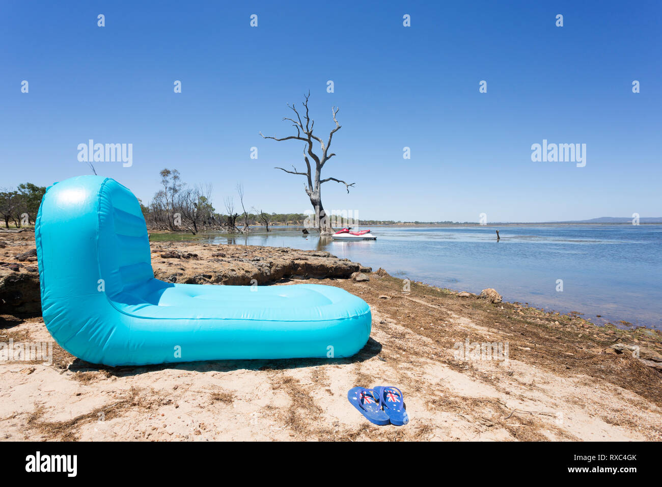 An inflatable pool toy at the side of a lake with Australian themed thongs in foreground Stock