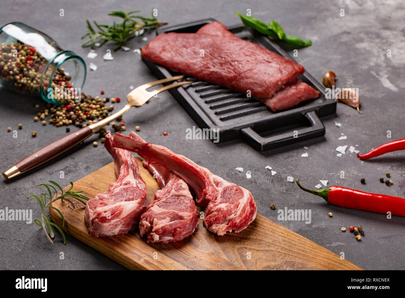 Set of Raw uncooked black angus beef tomahawk steaks on bones and veal tenderloin served with chilli and peppercorns. Rustic style. Close up Stock Photo