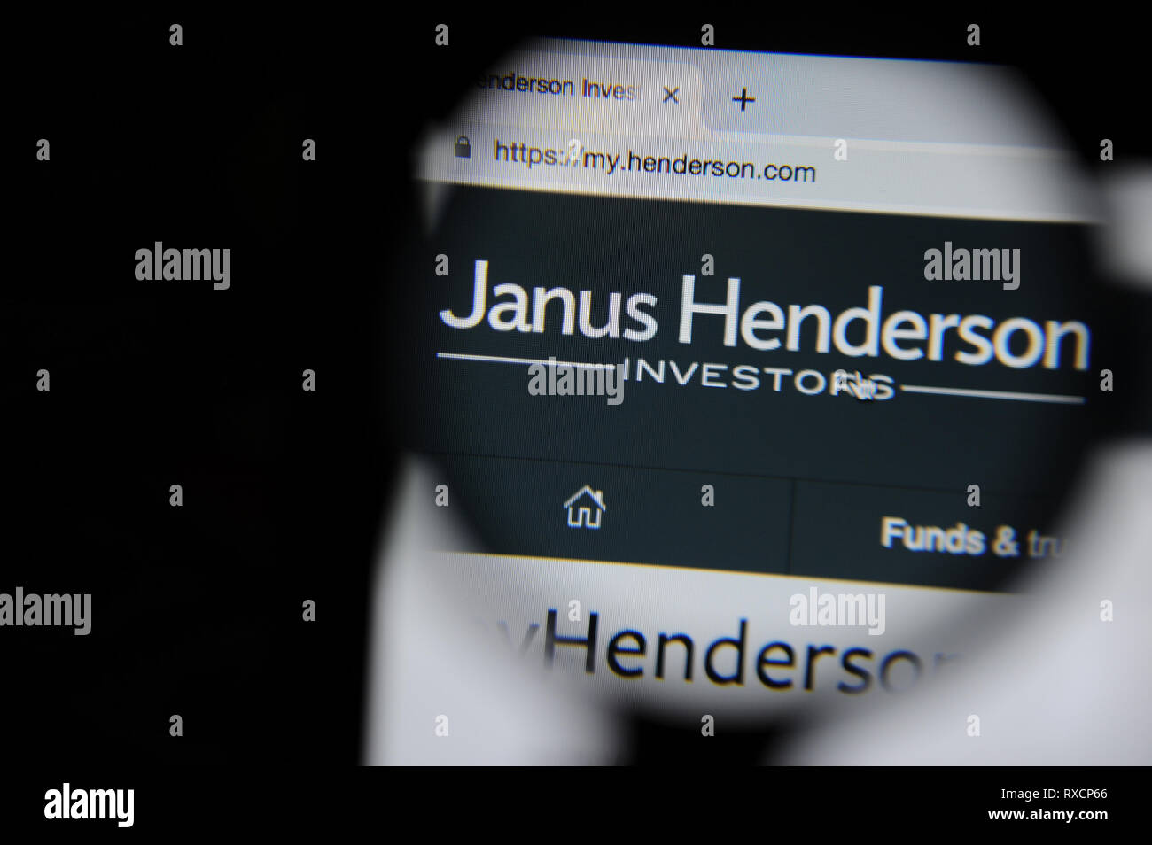 The Janus Henderson website is seen through a magnifying glass.  Janus Henderson formed in 2017 when Janus Capital Group and Henderson Global Investor Stock Photo