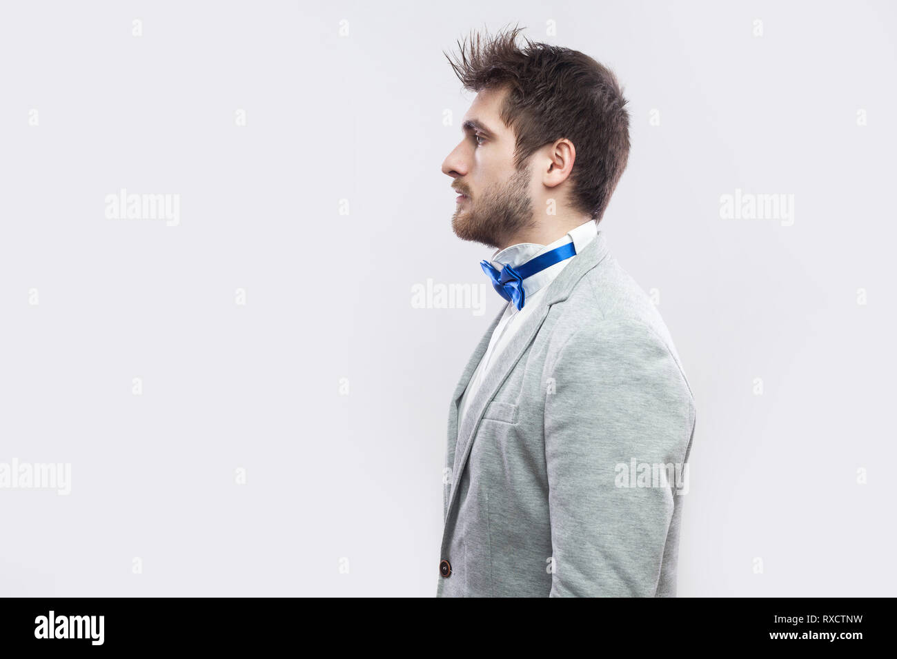Profile side view portrait of serious handsome bearded man in casual grey suit, blue bow tie standing and looking straight wih calm serious face. indo Stock Photo