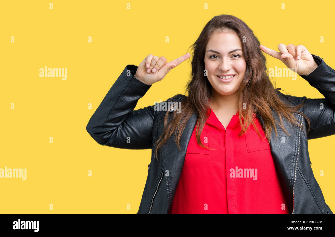 Beautiful plus size young woman wearing a fashion leather jacket over isolated background Smiling pointing to head with both hands finger, great idea  Stock Photo