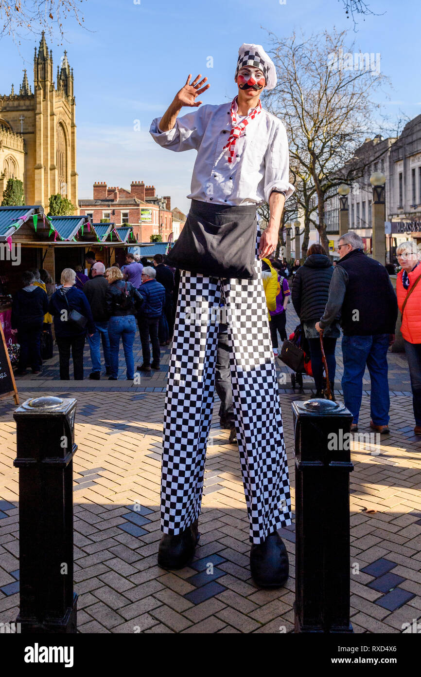 Super-sized chef (man on stilts) waving at camera, by trade stalls & people at Wakefield Food, Drink & Rhubarb Festival 2019, Yorkshire, England, UK. Stock Photo