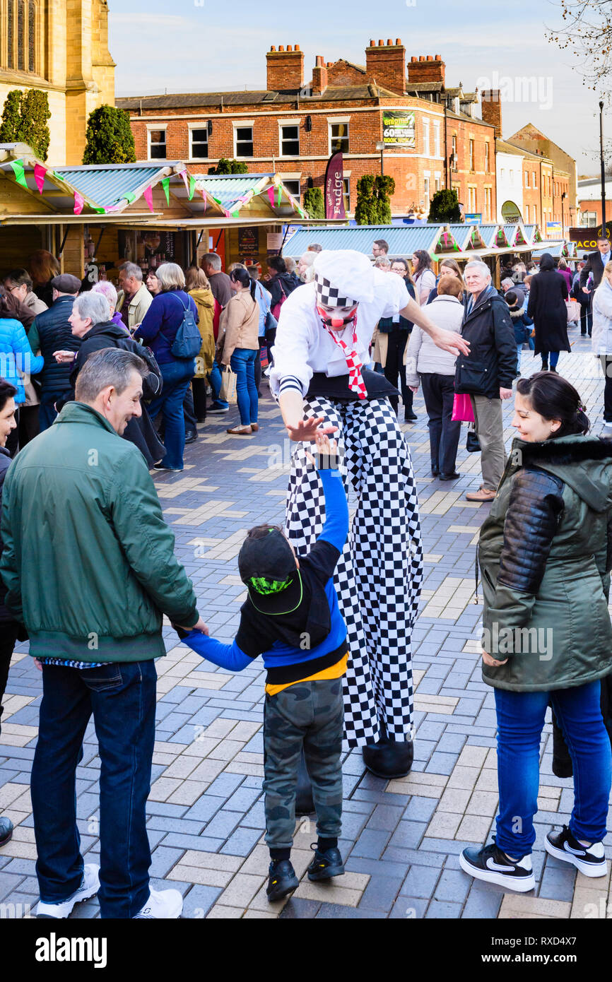 Super-sized chef (man on stilts) shares high five with small boy in crowd - Wakefield Food, Drink & Rhubarb Festival 2019, Yorkshire, England, UK. Stock Photo