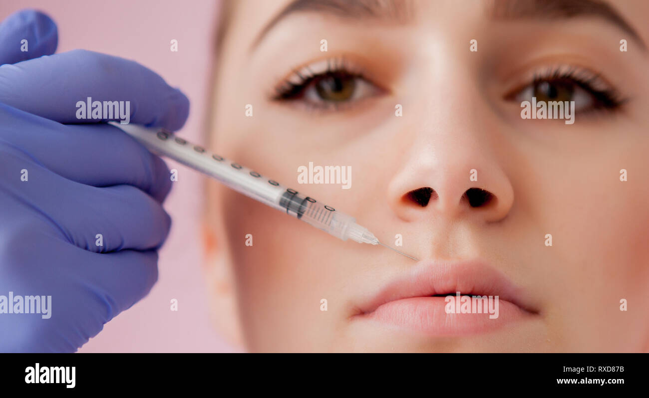 Doctor in gloves giving woman botox injections in lips, on pink ...