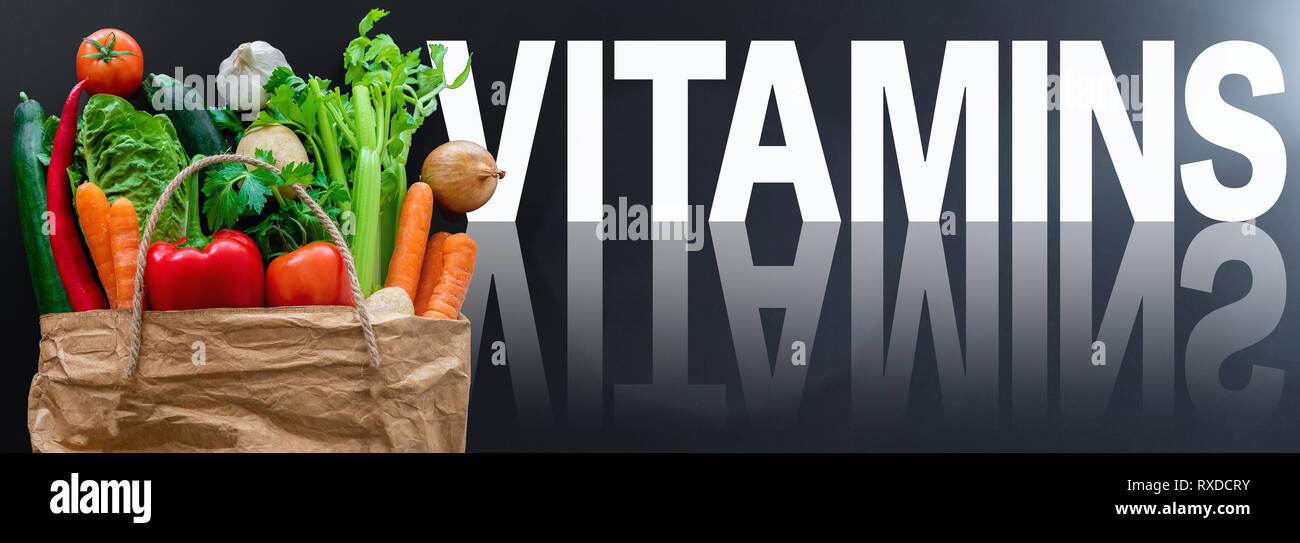 word VITAMINS against dark background with fresh healthy organic vegetables in paper bag Stock Photo