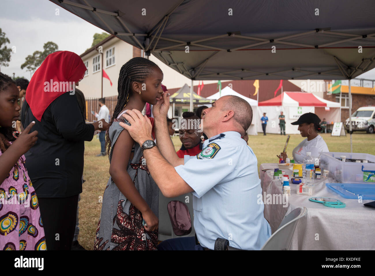 Sydney, Australia 9th, March 2019, NSW Police Sergent Robert Bourgault helps out with face painting at the Africultures Festival held in Wyatt Park, Lidcombe, Sydney. Despite the occasional shower of rain event goers were treated to music and entertainment, colourful market stalls and food from many of the represented nations. Contributor: Stephen Dwyer / Alamy Stock Photo Credit: Stephen Dwyer/Alamy Live News Stock Photo