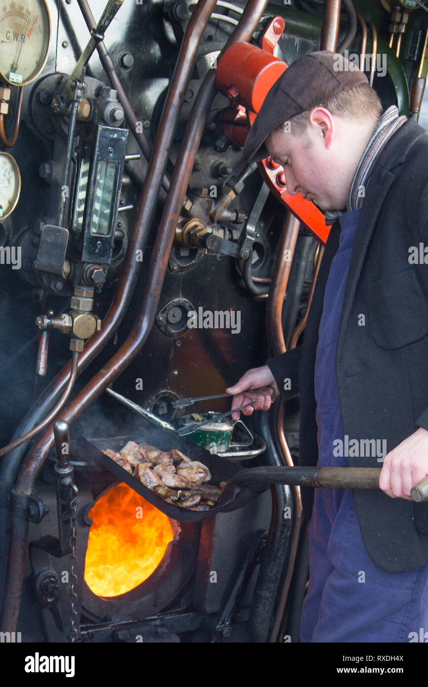 Kidderminster, UK. 9th March, 2019. Despite the sunny spells, it's a cold and windy March morning in the Midlands. A kind-hearted steam railway train driver stands on the footplate cooking up hot sausages and bacon baps for his crew in this vintage engine's firebox. As the crew heads out for the day, standing in the open locomotive cab, their hot breakfast baps will certainly help keep out the chilly winds they will be facing. Credit: Lee Hudson/Alamy Live News Stock Photo