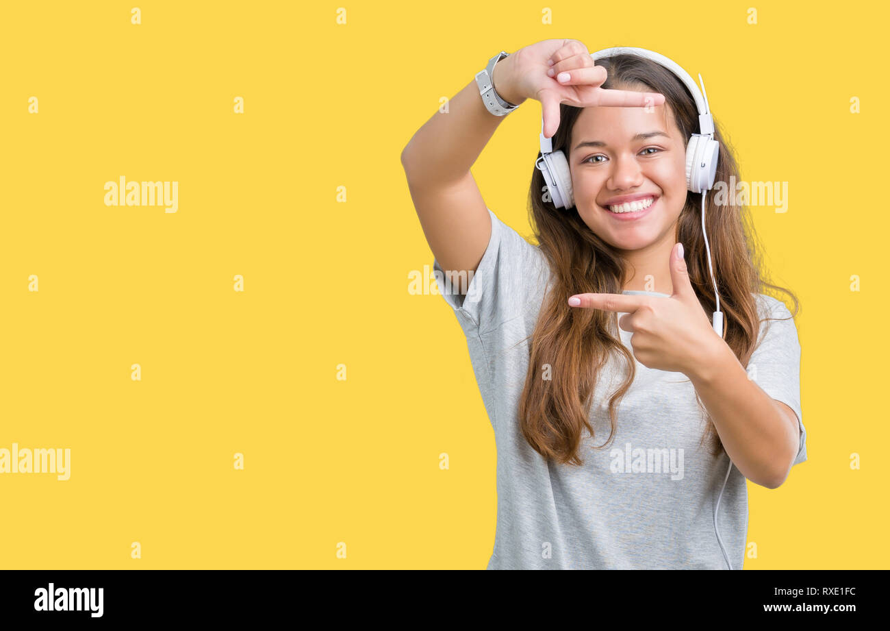 Young beautiful woman wearing headphones listening to music over isolated background smiling making frame with hands and fingers with happy face. Crea Stock Photo