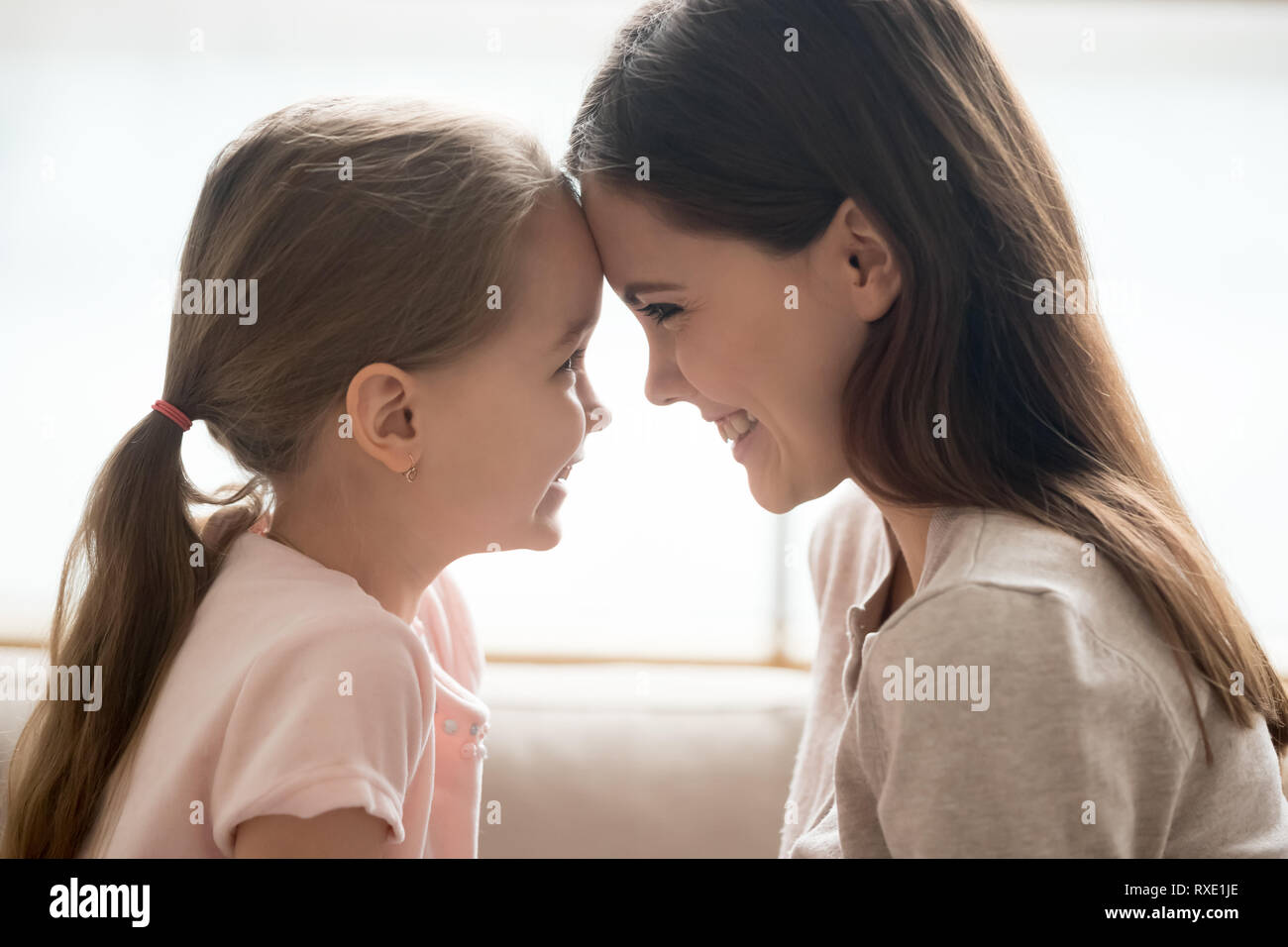Happy kid girl and smiling mother touching foreheads, side view Stock Photo