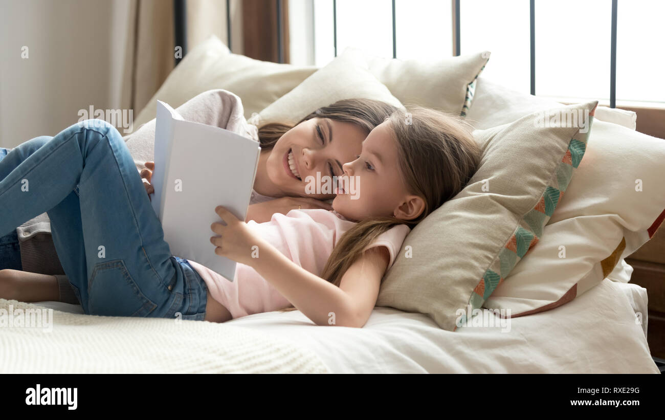 Cute child daughter holding book reading to mom in bed Stock Photo