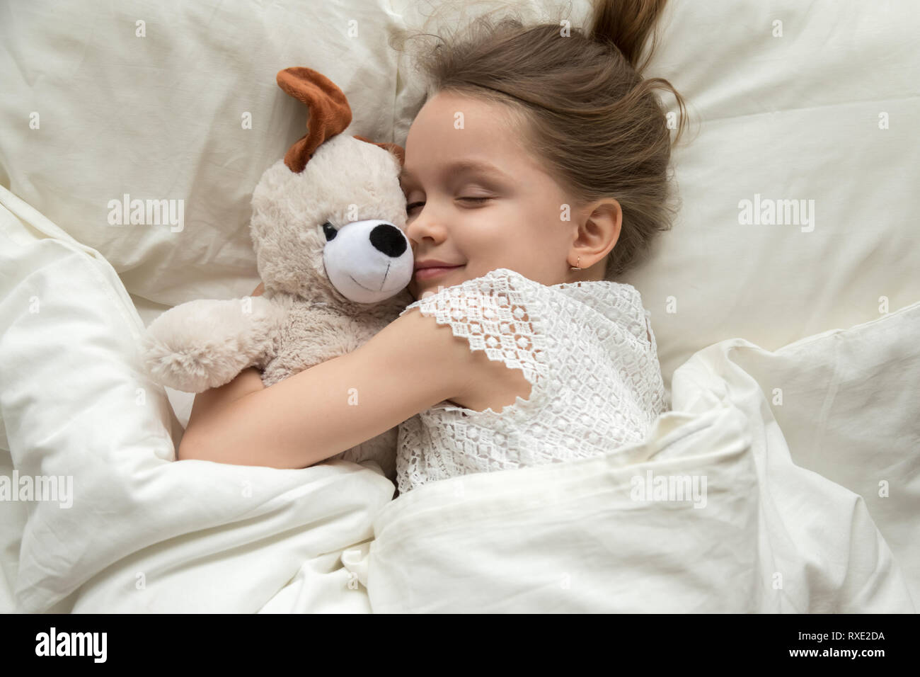 Cute little kid girl hugging teddy bear sleeping in bed Stock Photo
