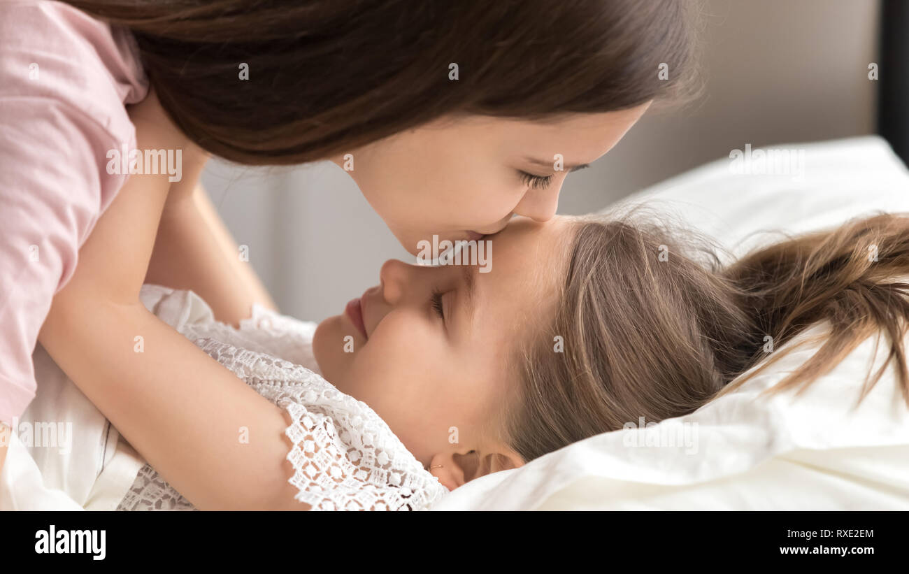 Loving mother kissing cute kid daughter waking up in morning Stock Photo