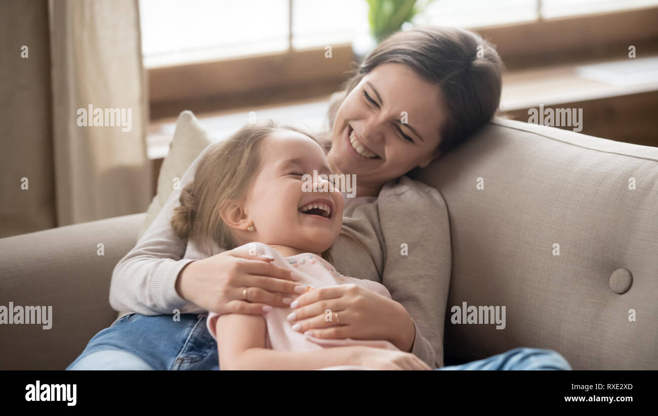 Happy mom embracing kid daughter laughing together lying on couch Stock Photo
