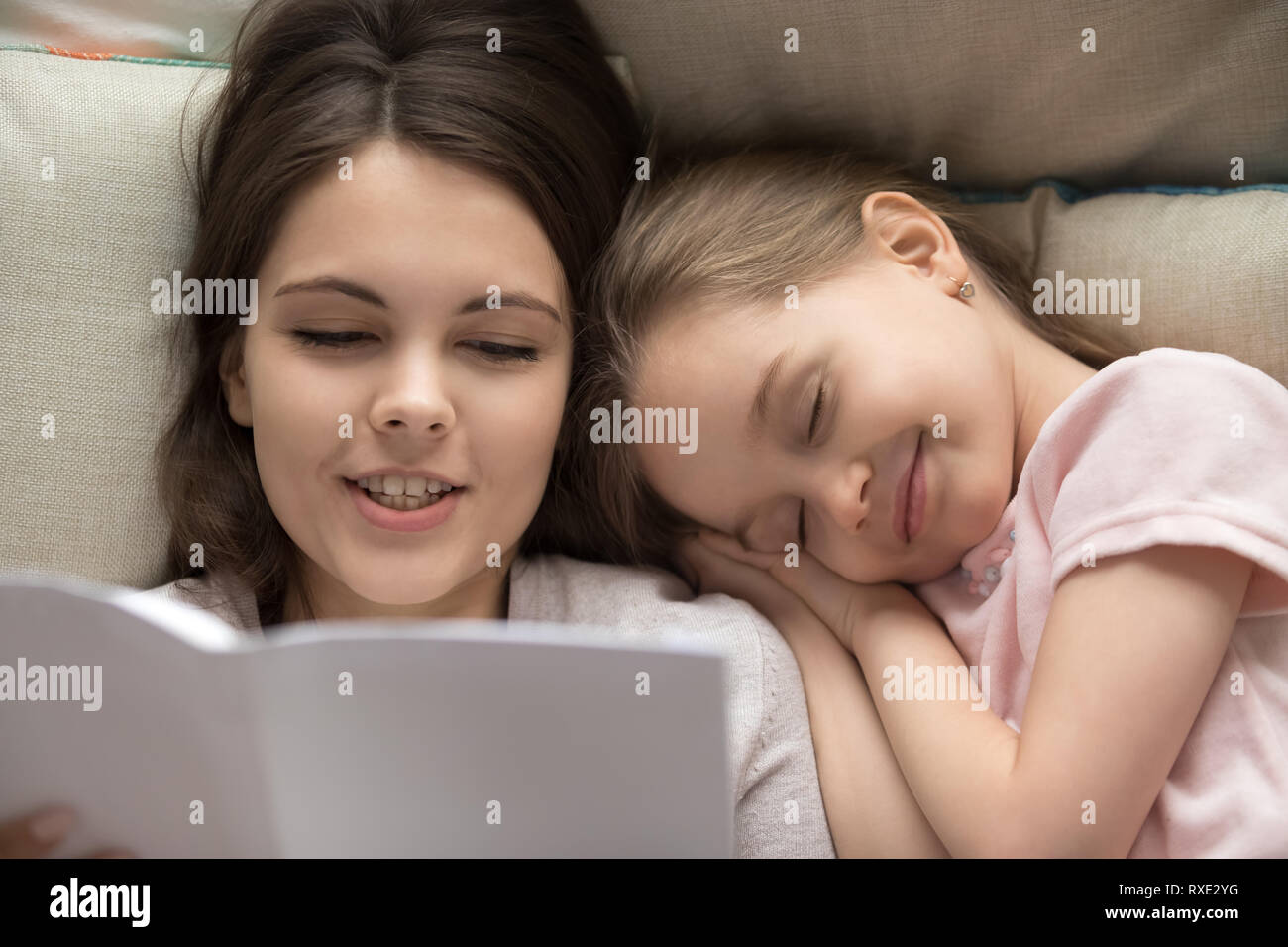 Happy little girl falling asleep in bed mum reading book Stock Photo