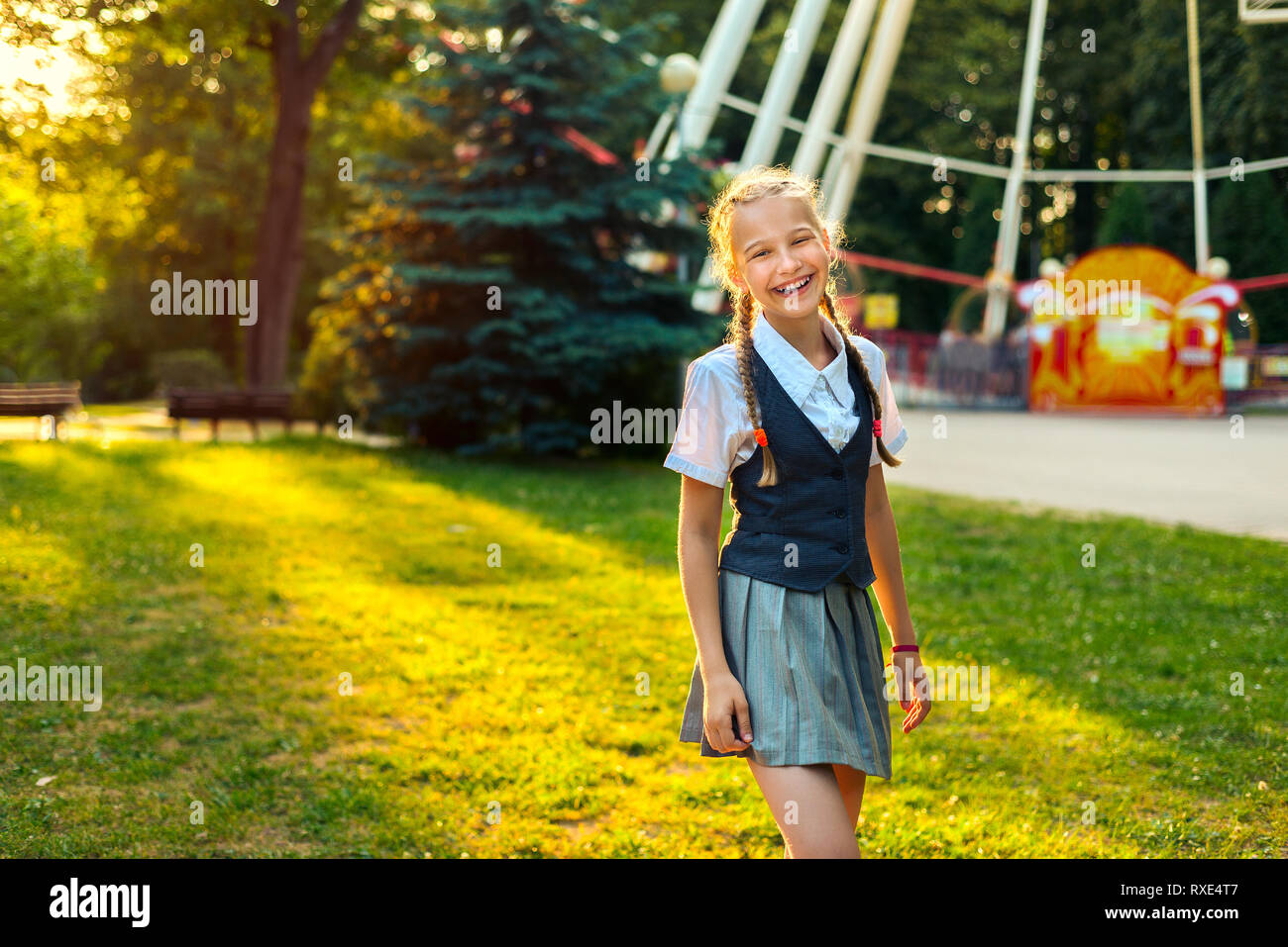 Portrait of schoolgirl in uniform laughing and rejoicing in summer in park at sunset in sunlight Stock Photo