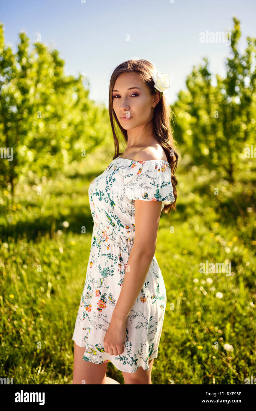 Pretty brunette girl is standing in a green dream-like orchard dressed in  flower summer dress Stock Photo - Alamy