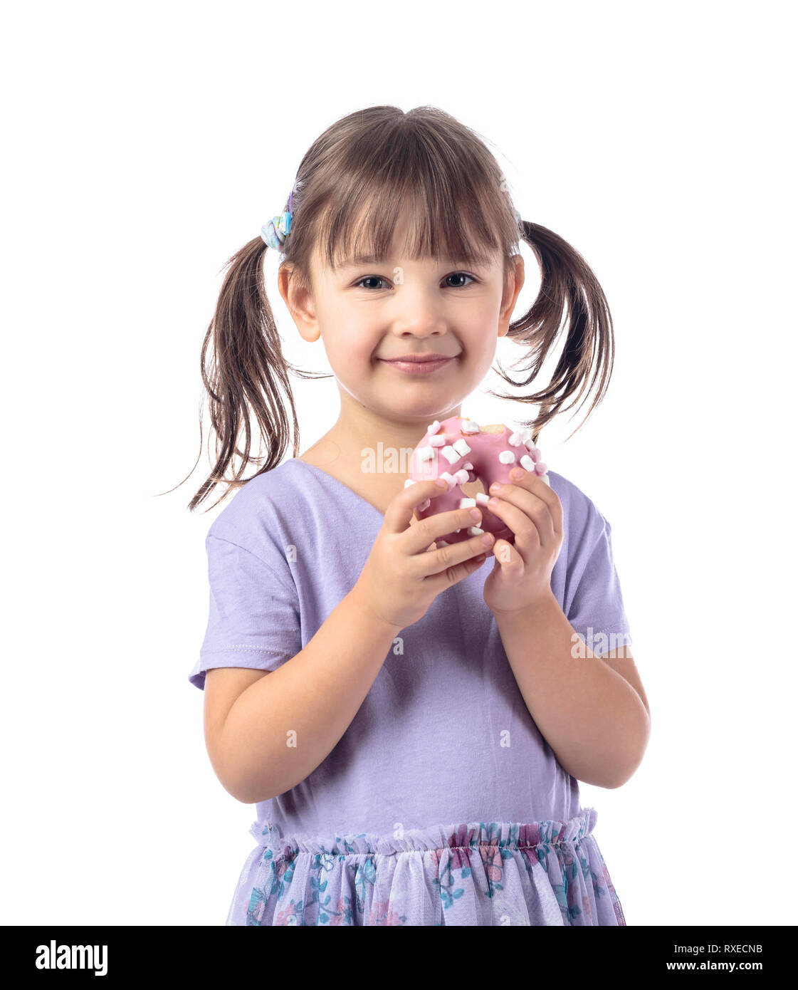 Four-year-old girl in a purple t-shirt eat donut.The girl's hair is tied in tails. Isolated on white background. Stock Photo