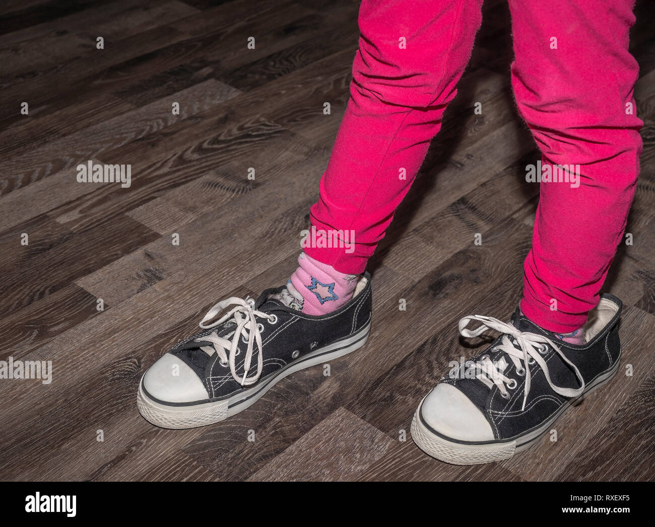 The girl carries a pair of larger sneakers and poses a kicking one leg a little ahead Stock Photo