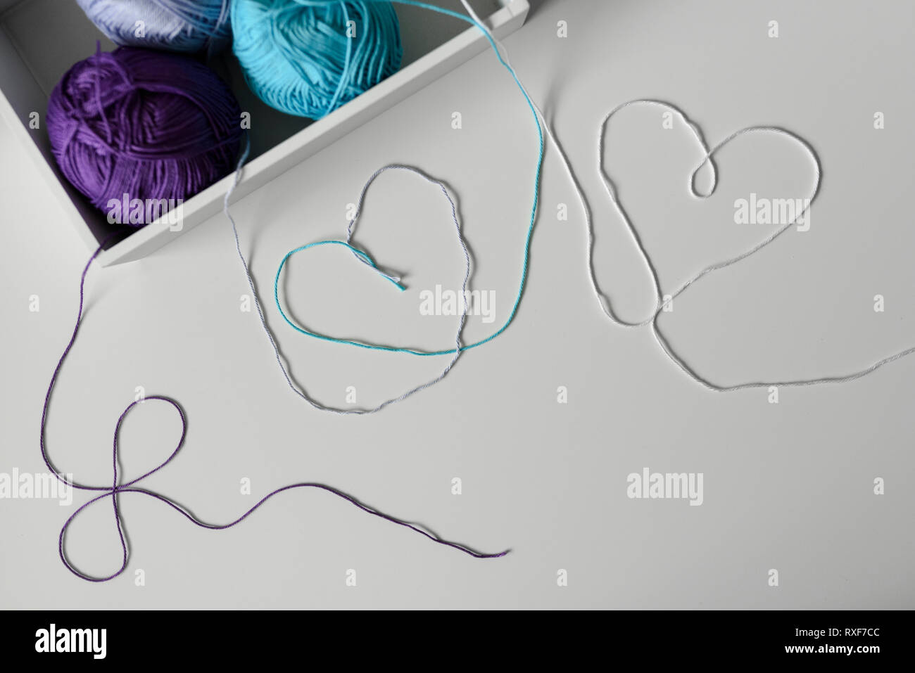 View from above on creative designed hearts from colorful wool strands coming out of the white box with knitting yarn balls. Stock Photo