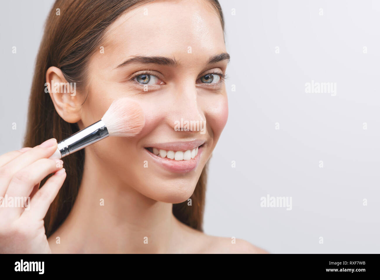 Young girl applies powder on the face using makeup brush Stock Photo