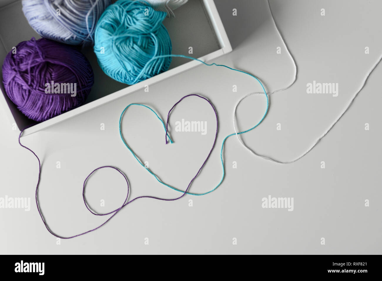 Creative and romantic way of design a love word with heart on white background from colorful threads coming out from wood box with knitting wools. Stock Photo