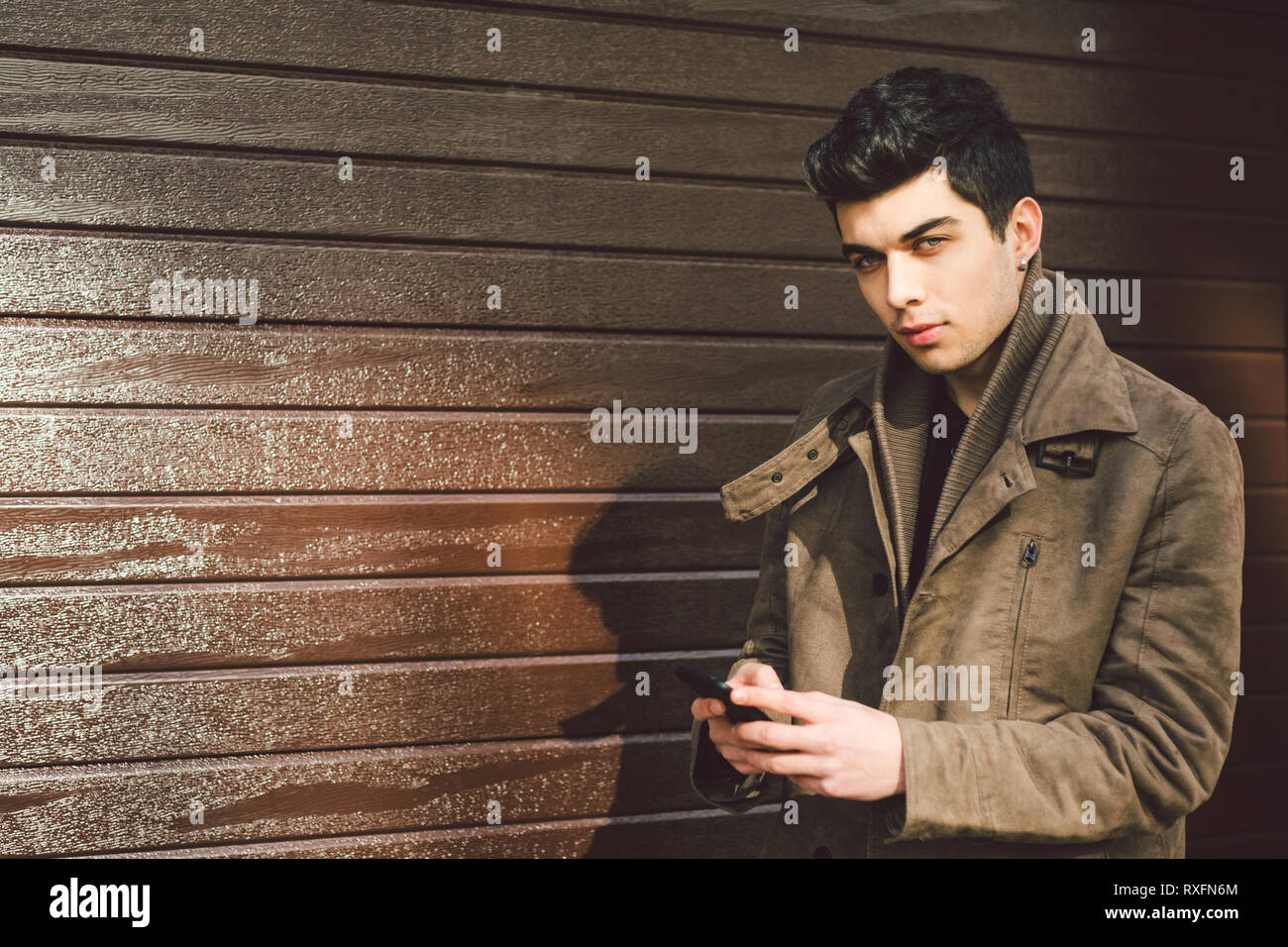 Portrait of young handsome Turkish male model of Mediterranean race brunet  in leather coat using hand phone of technology businessman on street in sun  Stock Photo - Alamy