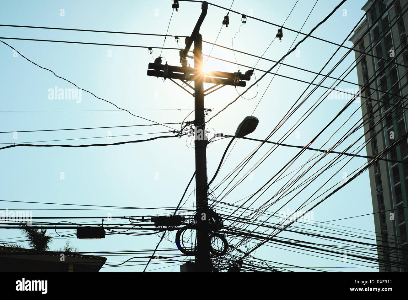 Low angle view of concrete post for street lamp and electric wires at dusk. Thick network of cables in silhouette hanging on a pole in Panama City. Co Stock Photo