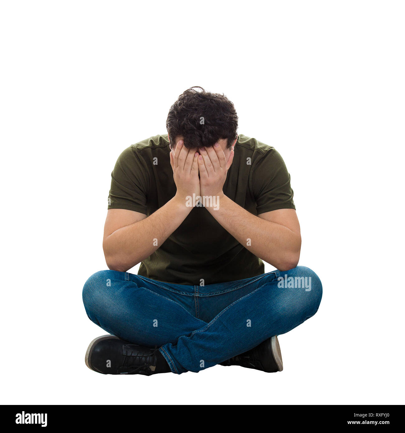 Upset and stressed young man wearing casual jeans and t-shirt, sitting on the floor with crossed legs, covering his face with both hands feel sad isol Stock Photo