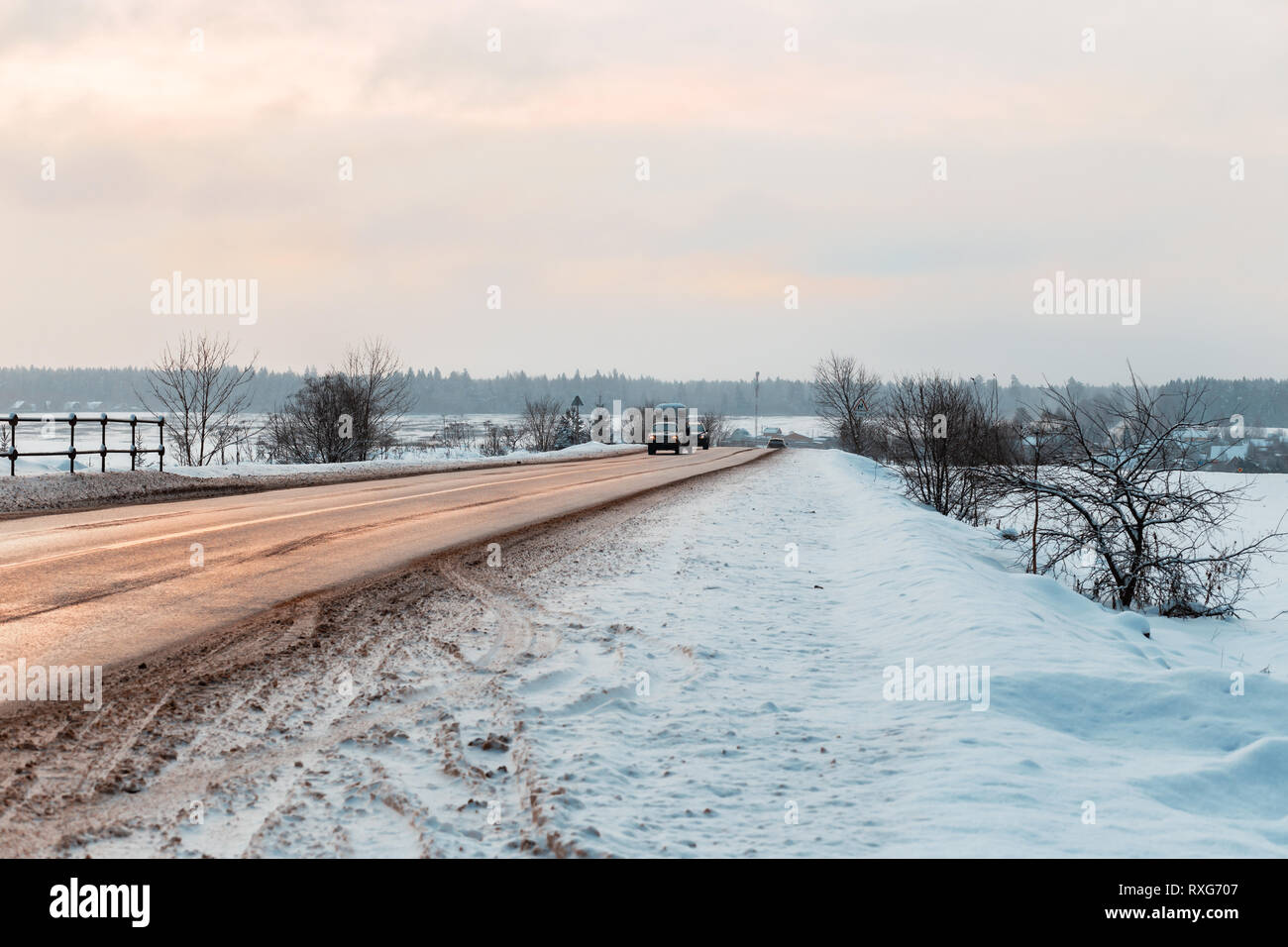 Winter road among the fields in the countryside. Reflection of the sun in the asphalt, sand on the roadsides and open spaces in the snow Stock Photo