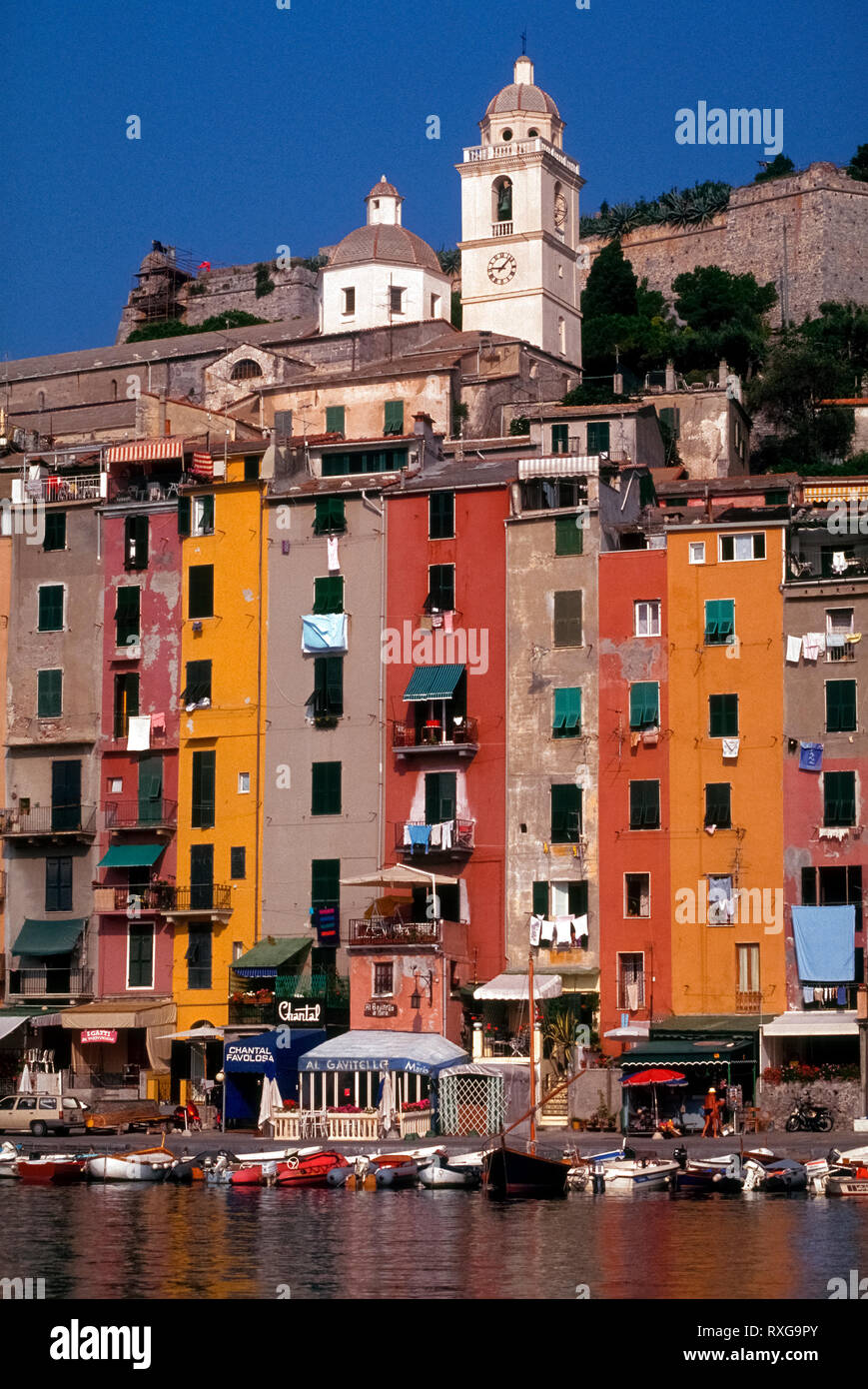 Multicolored facades marked by windows, shutters, balconies, and laundry hung out to dry decorate the vertical dwellings that overlook the boat harbor at Portovenere, Italy. Strong sunshine along the Mediterranean seacoast is a cause for frequent repainting of the exterior walls of these attached residences. This medieval fishing village on the Italian Riviera is among the most picturesque but lesser-known tourist towns in the Liguria region. Stock Photo