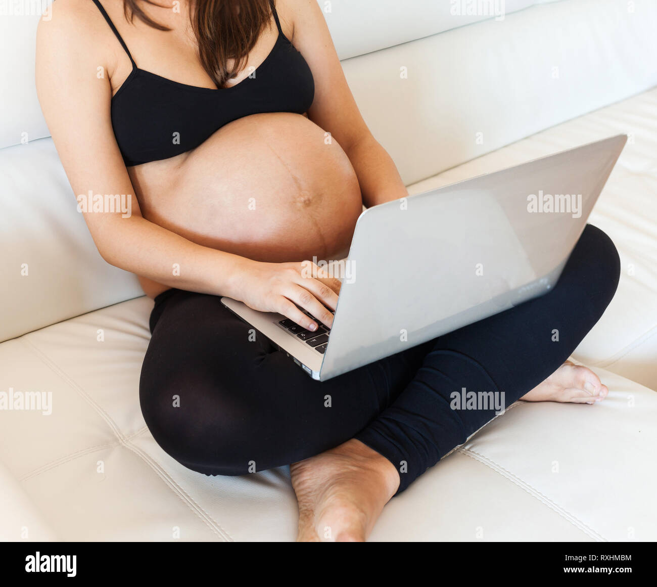 Pregnant woman with belly using a laptop on the sofa Stock Photo